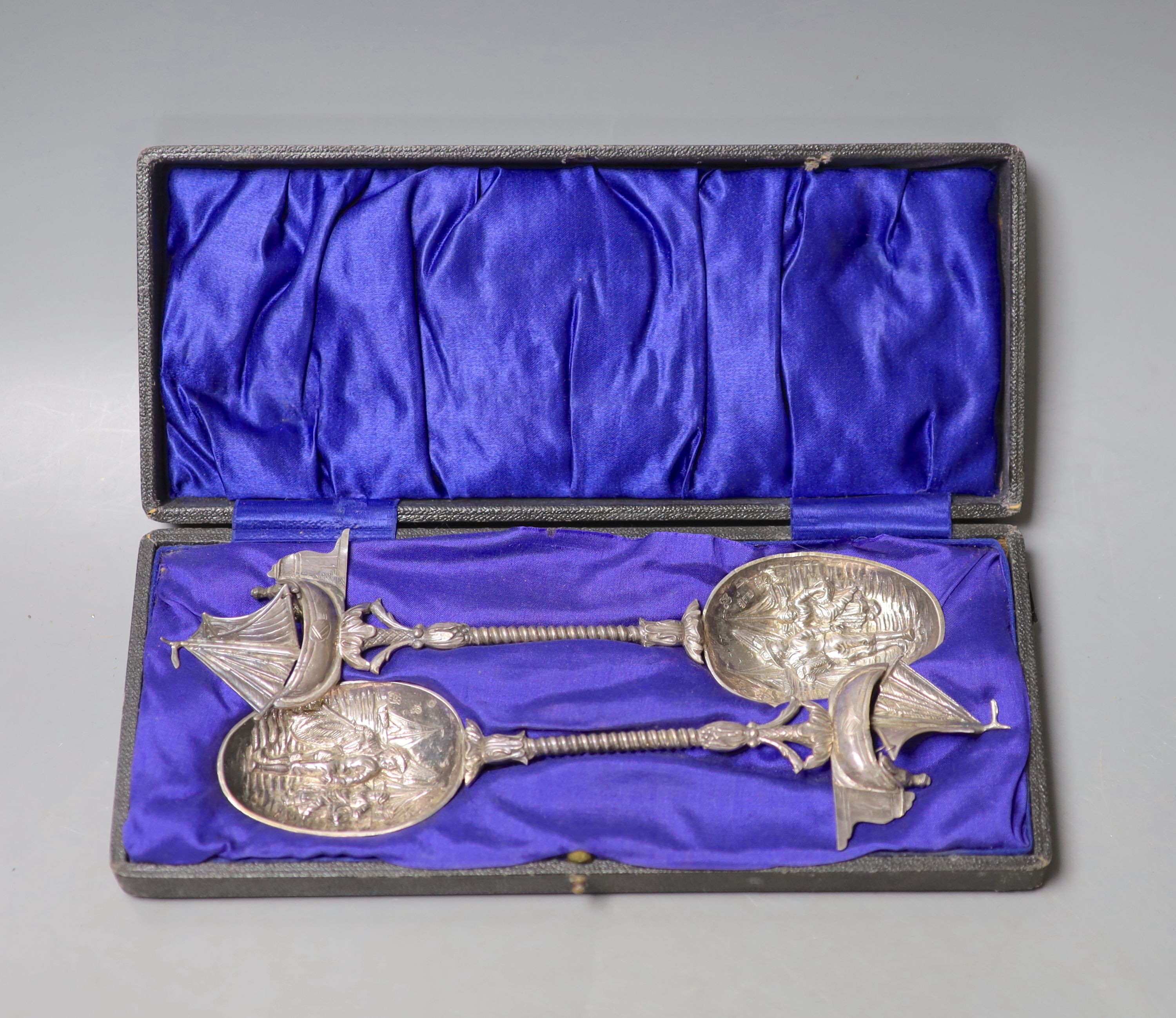 A cased pair of early 20th century Hanau white metal serving spoons, with embossed bowls and yacht terminals, with Dutch import marks, 21.5cm, 165 grams.